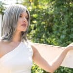Woman with silver-gray wig outdoors, natural sunlight, lush green background.